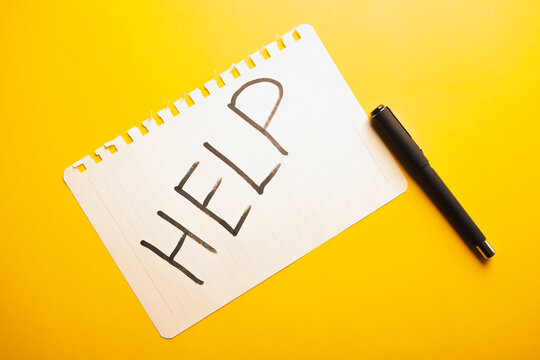 The word help is written in a notebook on a yellow background.