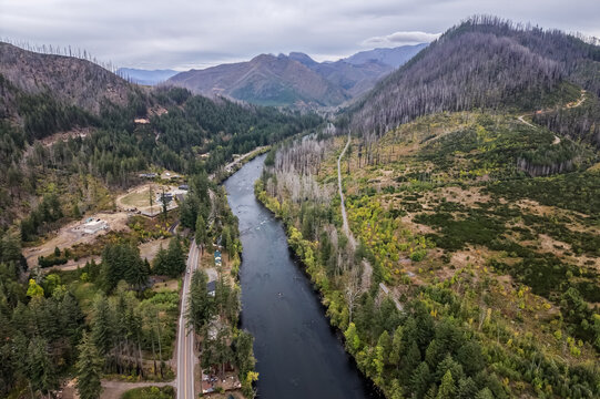 Aerial view of the McKenzie River flowing through a landscape marked by burn scars on the surrounding hillsides, with a road running alongside the river in Vida, Oregon, United States.