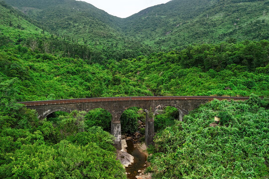 Sturdy stone railway bridge arching over a small mountain stream nestled deep within the vibrant evergreen rainforests of the majestic Hai Van Pass