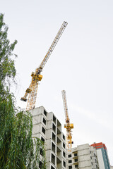 Tall yellow construction crane towering over multi-story building site A tall yellow tower crane working at a high-rise residential building construction site against an overcast sky. Concrete structu © Karina