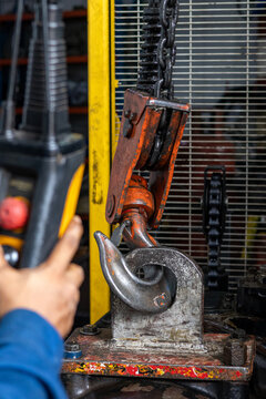 Operator controls overhead electric chain hoist crane lifting heavy machinery bracket in workshop.
