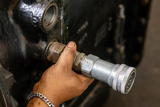 Mechanic installs quick disconnect hydraulic coupler into heavy machine port inside repair workshop.