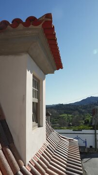 Vertical 4K video showing a traditional wooden dormer window on a clay tile roof with a scenic countryside view under a blue sky