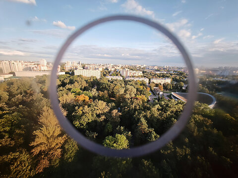Aerial view of a city, buildings, and abundant green trees, seen through a defining circular element