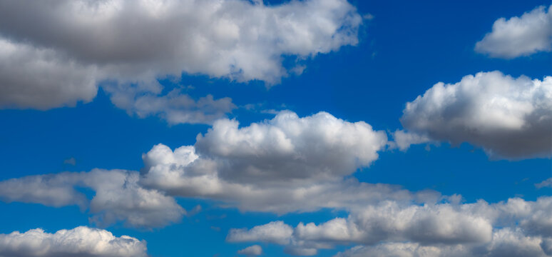 Wide panoramic view of large white and grey cumulus clouds against an intense blue summer sky, creating a vivid and atmospheric natural background.