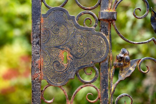 Close-up of an ornate weathered wrought iron gate with decorative scrollwork and floral details in the park of Holkham Hall, Norfolk, England.