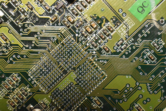 High angle full frame background texture of an electronic motherboard featuring intricate circuitry, resistors, transistors, and a quality control stamp.