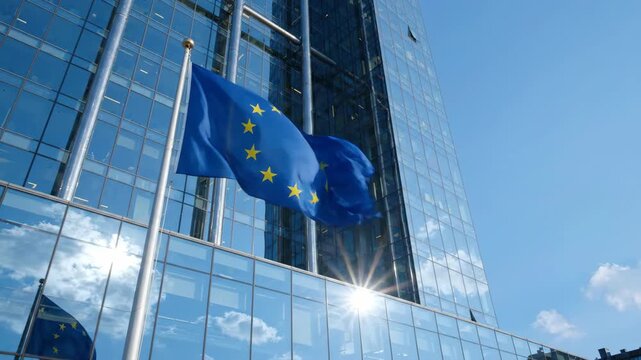 European Union flag waving proudly in front of a modern glass skyscraper under a clear sky.