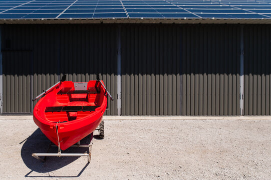 A red fishing and recreational boat on a trailer, set against a metallic gray hangar. Minimalism with a bold splash of color against a gray background. Summer outdoor recreation. solar panels on roof