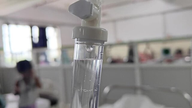 Close-up of a medical IV drip chamber with saline solution in a hospital ward