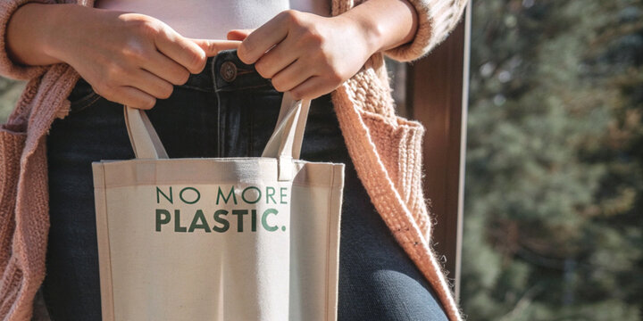 Eco friendly lifestyle with waste reduction with a woman carrying a canvas bag that has the slogan NO MORE PLASTIC