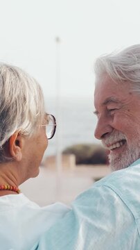 Back view of a mature couple in love, with the man affectionately placing his arm around his wife while they both smile and gaze lovingly at each other, enjoying the beautiful sea view