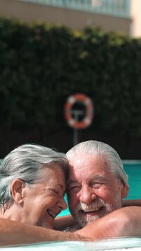 Happy senior couple relaxing and having fun together in a swimming pool, laughing and enjoying their summer vacation. Elderly man and woman showing affection and love while swimming