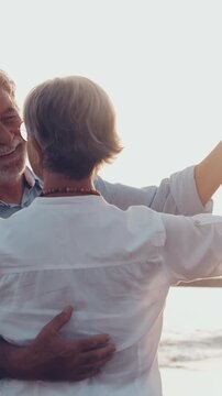 Happy mature couple romantically dancing together in slow motion on the beach during a beautiful sunset, sharing a tender and loving moment during their retirement vacation