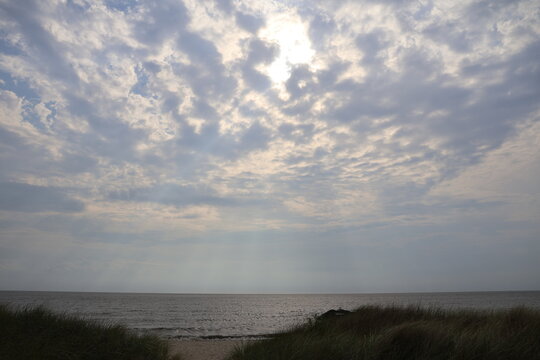 A dreamlike sky with clouds thinly veiling golden sunlight from above; casting a glow over the calm bay water of North Cape May.