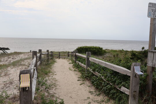 A footpath etched into the sand dunes, sloping down to a beachhead of the Cape May Bay on a quiet summer evening.