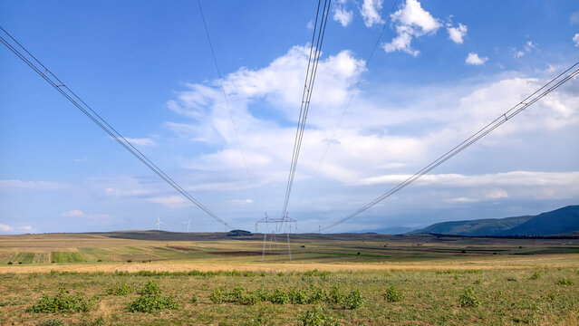 High voltage power lines transmitting essential electricity across a rural landscape, symbolizing energy infrastructure, modern development, and sustainable power generation with wind turbines