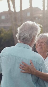Happy senior couple enjoying retirement, dancing slowly and romantically in a park during a beautiful sunset, smiling and looking into each other's eyes with love and affection