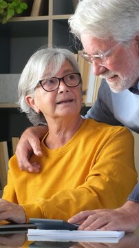 Cheerful mature retired couple using a laptop and calculator for online banking and financial planning, smiling while managing their household budget and investments from home