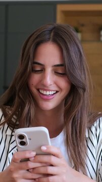 Beautiful happy woman holding her smartphone, texting a message to a friend, and smiling while reading the screen, showing contentment and joy from the received communication