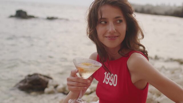 Enjoying a drink by the beach at sunset while wearing a red top with 1990 printed on it
