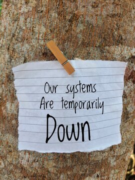 A handwritten note attached to a tree trunk stating that systems are currently down and temporarily out of service.