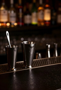 Mixology and cocktail preparation, metal shaker and jigger on a bar counter with blurred liquor bottles in a dark lounge for nightlife hospitality