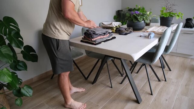 Man doing domestic chores folding clean clothes on a dining table in his modern home