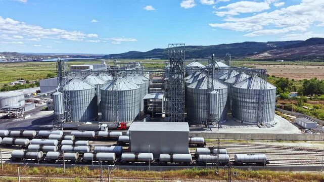 A grain storage facility with multiple silos and a railway line in the foreground. The area is located in a rural setting with fields in the background.