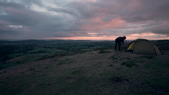 A man setting up his wild camping tent at dusk in the hills of England
