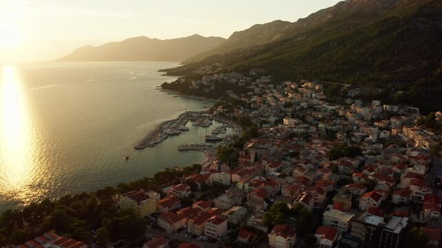 Coastal apartments and hotels offer summer vacation rentals in Baska Voda Croatia. Adriatic seaside resort properties welcome tourists at sunset. Real estate accommodations line harbor coast.