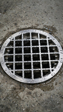 Close-up of stainless steel floor drain with water droplets on concrete factory floor