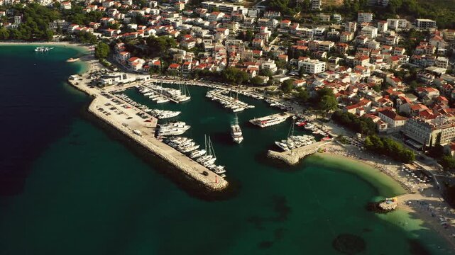 Baska Voda marina harbor shelters yachts along Makarska Riviera coast. Clear Adriatic Sea waters surround the resort town for Mediterranean sailing vacation and tourism in Dalmatia, Croatia.