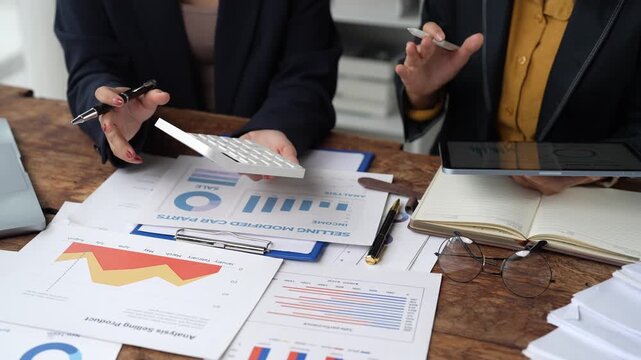 Businesswomen analyzing financial charts and discussing a marketing plan during a team meeting, using a calculator and digital tablet for data analysis and strategy
