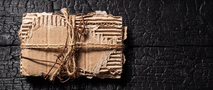 Rustic Cardboard Parcel Tied with Twine and Wire on Burnt Wood