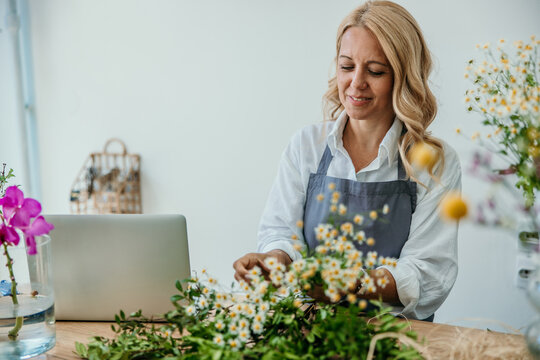 Female florist arranging flowers with laptop for small business