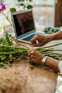 Florist hands tying fresh flower arrangement with laptop