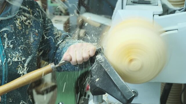 Woodturning on a wood turning lathe. Carpenter shaping a piece of wood into a bowl with a skew chisel, producing many wood curls. Design, art, carpentry, craftsmanship and manufacturing concept.	
