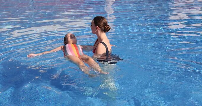 Swimming lesson. Coach teaching little girl to swim in pool. Camera moving backwards