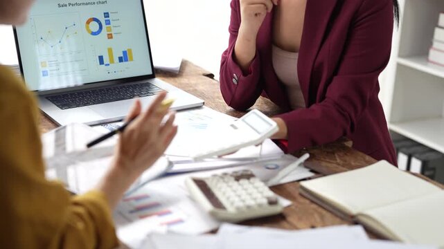 Businesswomen analyzing financial data and sales performance charts during a collaborative office meeting, focusing on strategic planning and budget calculation
