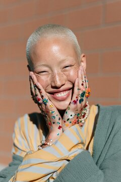 Natural outdoor portrait of person with short buzz cut and decorated hands smiling for lifestyle marketing and editorial portrait background
