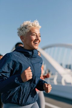Laughing young woman running on modern bridge urban fitness background for health banner and lifestyle design