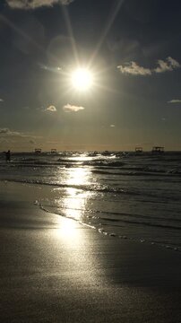 P&ocirc;r do sol dourado sobre o mar com ondas suaves e quiosques ao longe, cena rom&acirc;ntica de fim de tarde durante viagem &agrave; praia
