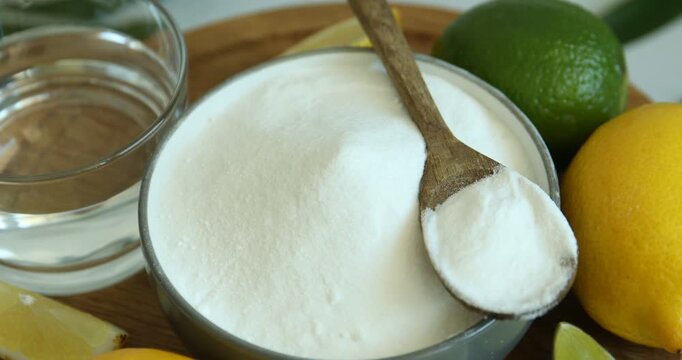 Baking soda in bowl, citrus fruits and water on wooden board, closeup