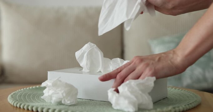 Woman taking paper tissue out of box at wooden table indoors, closeup