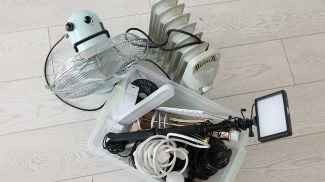 Plastic container with different broken appliances for recycling on floor indoors, flat lay. Camera moving in