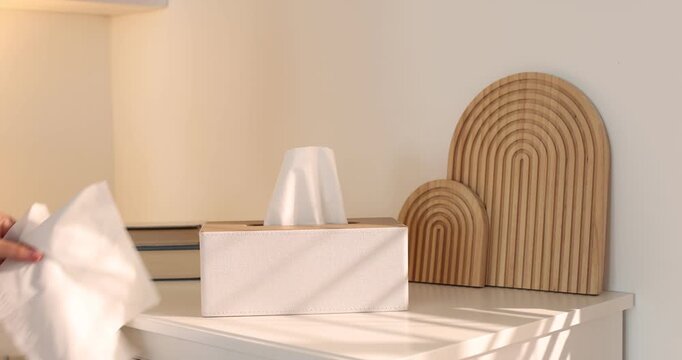 Woman taking paper tissues out of holder near cabinet indoors, closeup