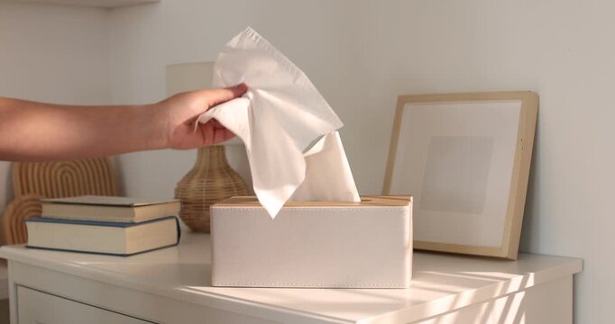 Woman taking paper tissue out of holder near cabinet indoors, closeup
