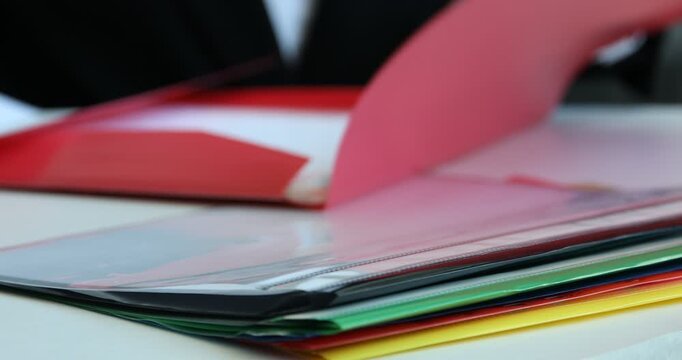 Businesswoman putting document into red file folder and placing it on stack of others at table, closeup. Selective focus