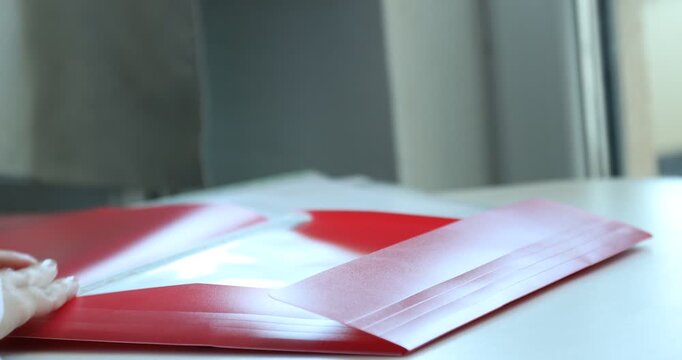 Businesswoman placing punched pocket with paper sheet into file folder at table, closeup